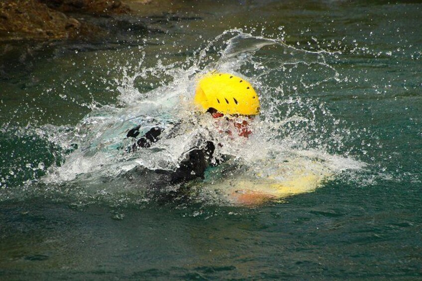 A person in a yellow helmet and wetsuit swimming in water. 4
