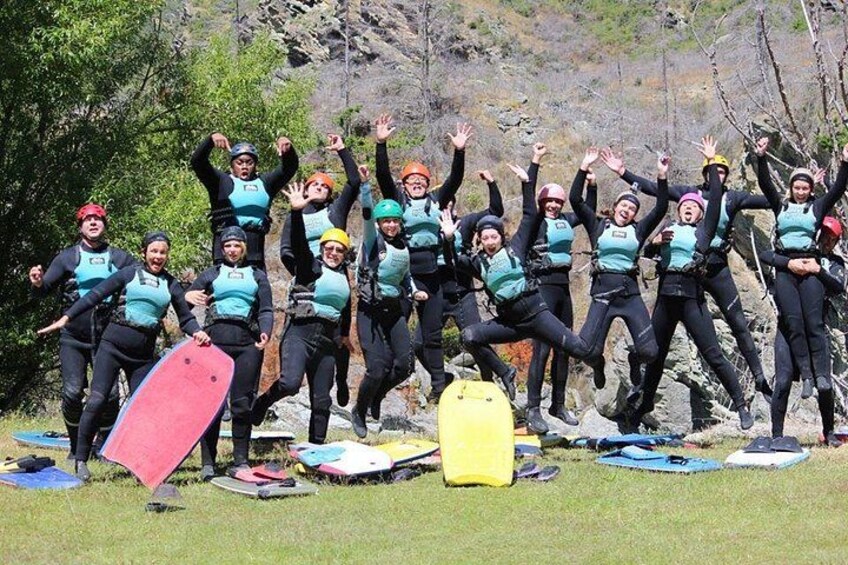 Un grupo de personas con trajes de neopreno y chalecos salvavidas en un campo de césped, con tablas de surf y un contenedor amarillo. 3