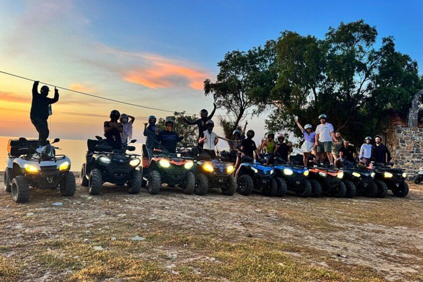 En gruppe mennesker på ATV'er står på rad og række på en jordvej med solnedgang i baggrunden. 5