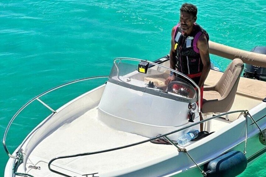 Ein kleines Boot mit einer Person, die eine Rettungsweste trägt, steuert durch ruhiges, blaues Wasser, im Hintergrund strahlender Himmel. 4