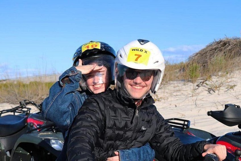 Two people on ATVs with helmets marked 'WILD X 7' and 'WILD X 10' on a sandy beach. 3
