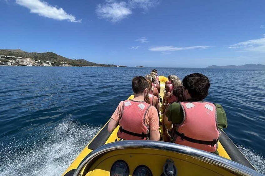 Un grupo de personas en un bote amarillo con chalecos salvavidas, navegando por un cuerpo de agua con una costa al fondo. 4