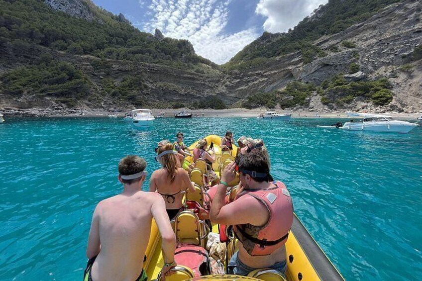 Un grupo de personas en un bote inflable amarillo en aguas azules y cristalinas, rodeado de acantilados rocosos y embarcaciones en la orilla. 3
