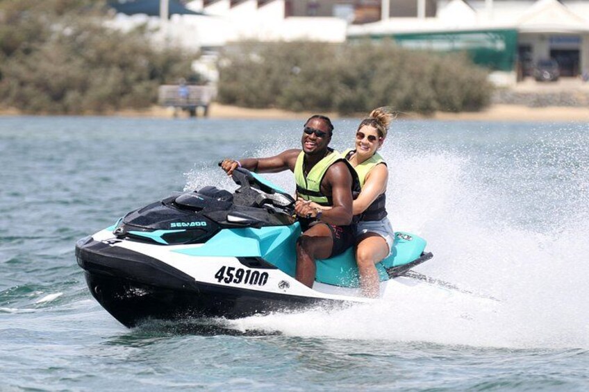 Twee personen op een jetski met het nummer 459100, die door het water scheren. 2