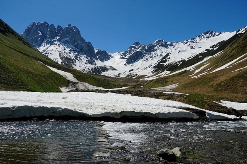 A mountain landscape with snow-covered peaks, a glacier, and a stream. 2