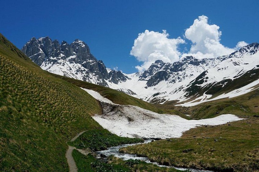 A mountain landscape with a snow-covered valley, a stream, and a clear sky. 3