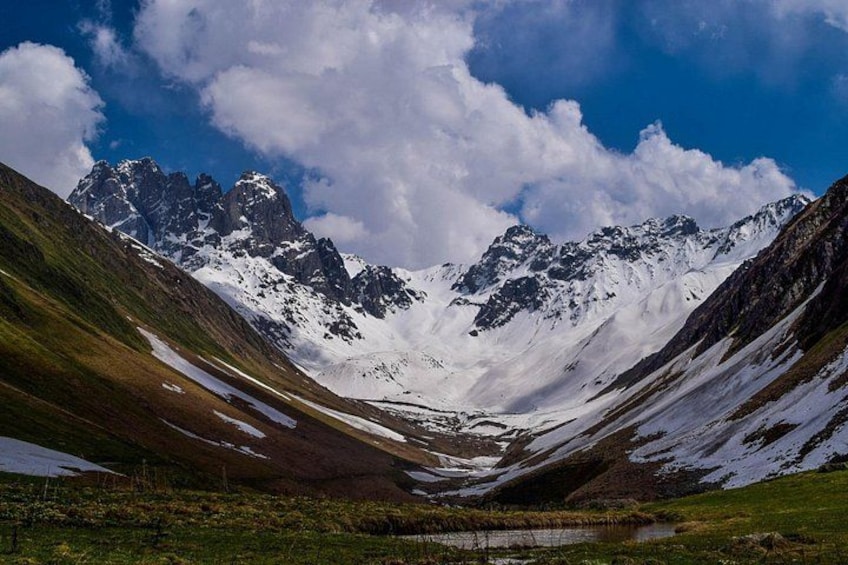 A mountain landscape with snow-covered peaks, a valley, and a small body of water. 4