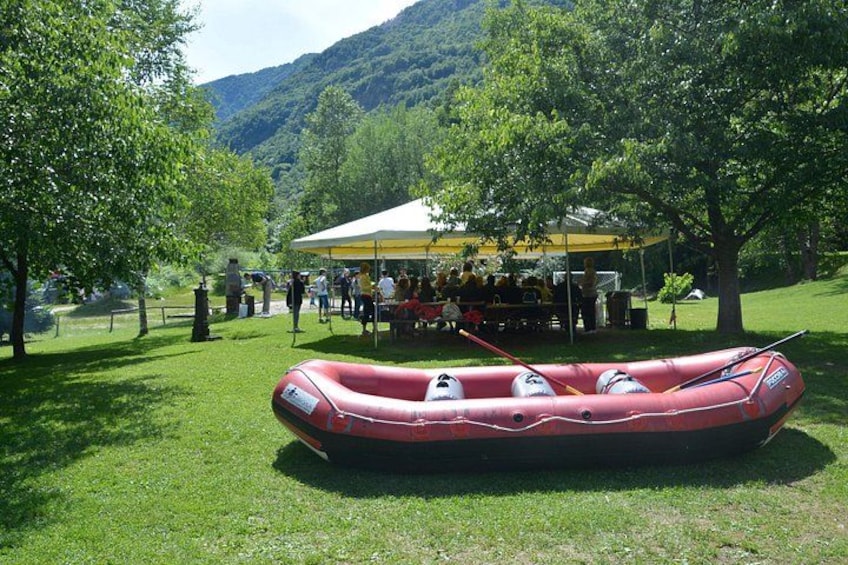 Una balsa hinchable roja sobre césped, con una tienda de campaña y personas al fondo. 2