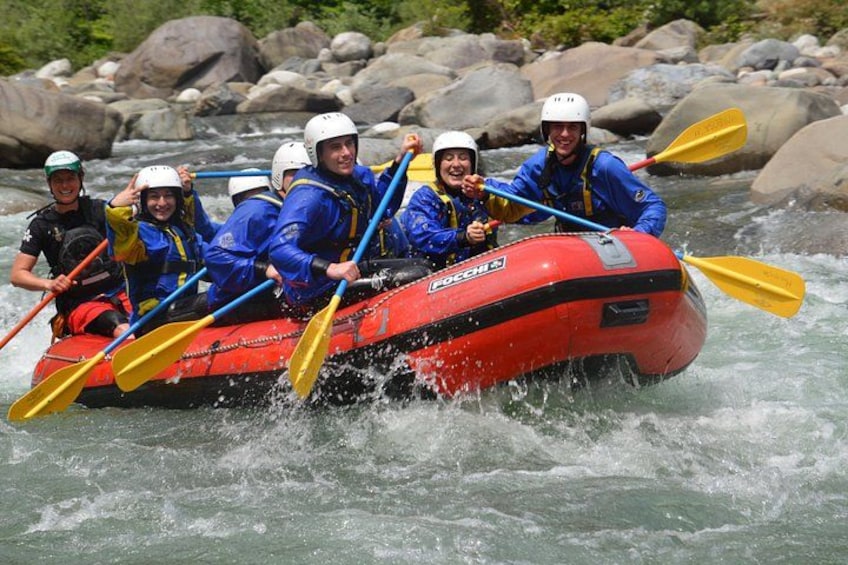 Un grupo de personas en un bote inflable rojo en un río, con rocas al fondo. 1