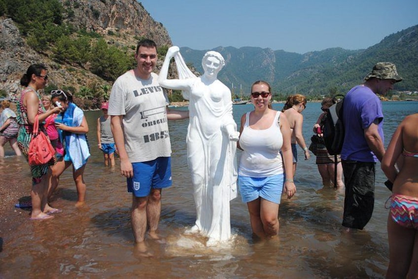 A group of people standing near a white statue in shallow water, with mountains in the background. 5