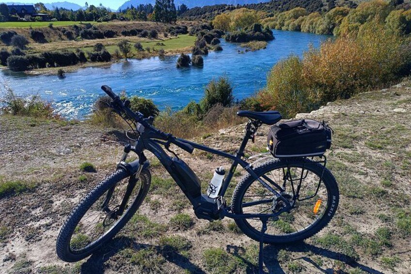 A mountain bike with a water bottle and a bag, parked on a grassy area near a river. 4