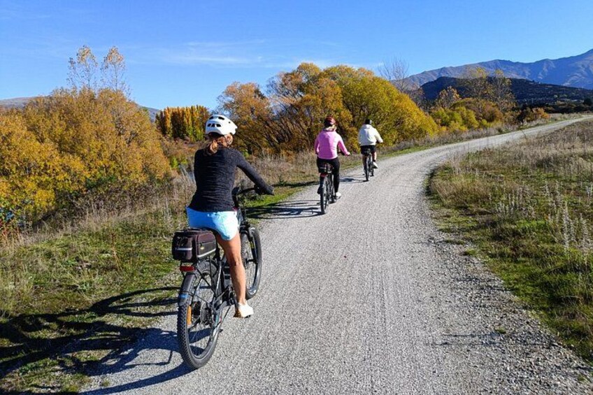 Three cyclists on a gravel road with autumn foliage and mountains in the background. 5