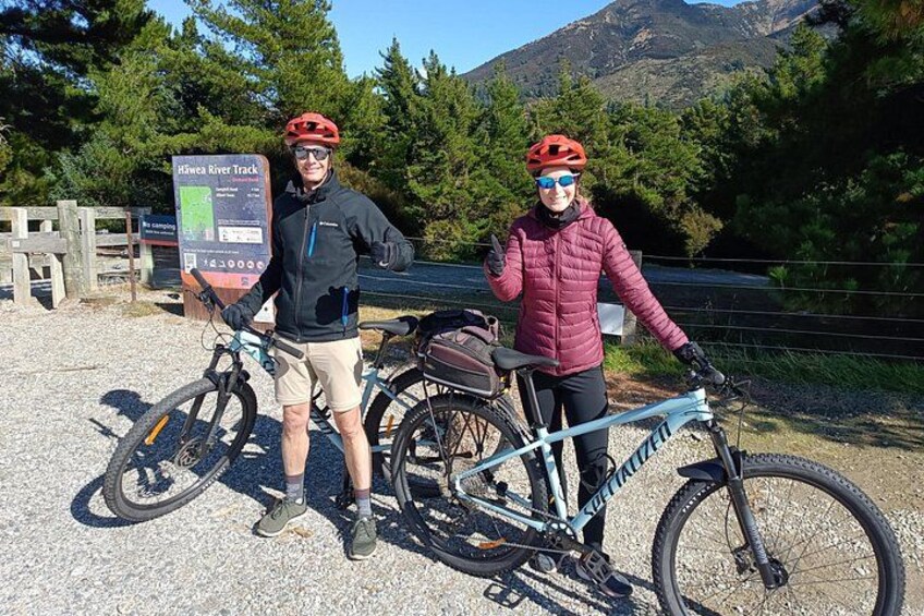 Two cyclists with bicycles, a signboard, and a mountainous landscape. 2