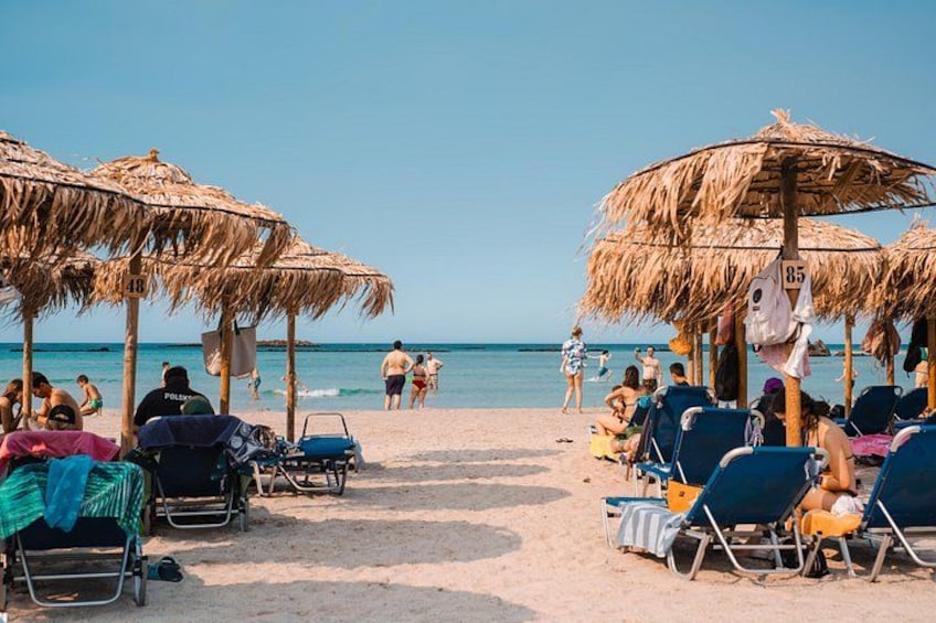 En strand med parasoller av halmtak, solstolar och folk som solar. 2