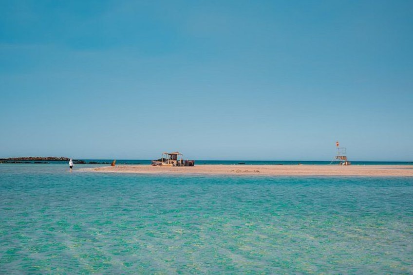 En strand med kristallklart turkost vatten, ett livräddartorn och ett litet fordon på sanden. 3