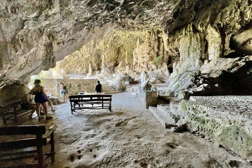 A cave interior with stalactites, a wooden bench, and visitors. 5