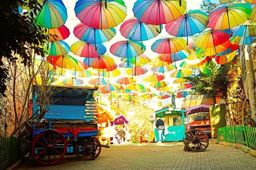 Una calle con paraguas de colores colgando, un carrito rojo y azul, y un carrito verde. 2