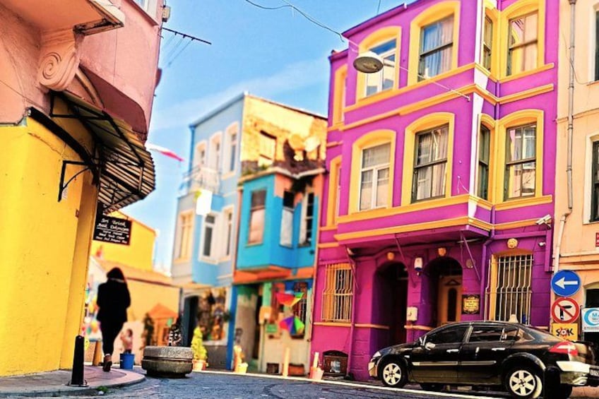 A street with colorful buildings, a parked car, and a person walking. 4
