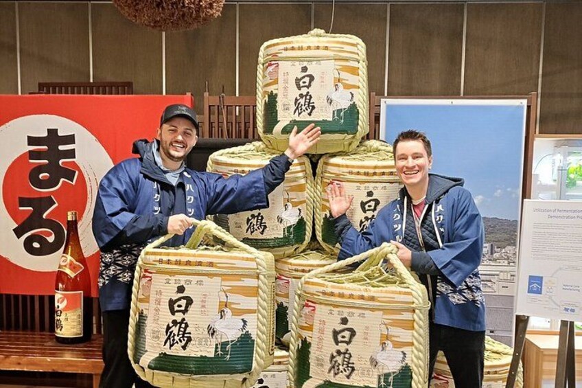 Two people standing in front of large bags of rice with Japanese characters on them. 1
