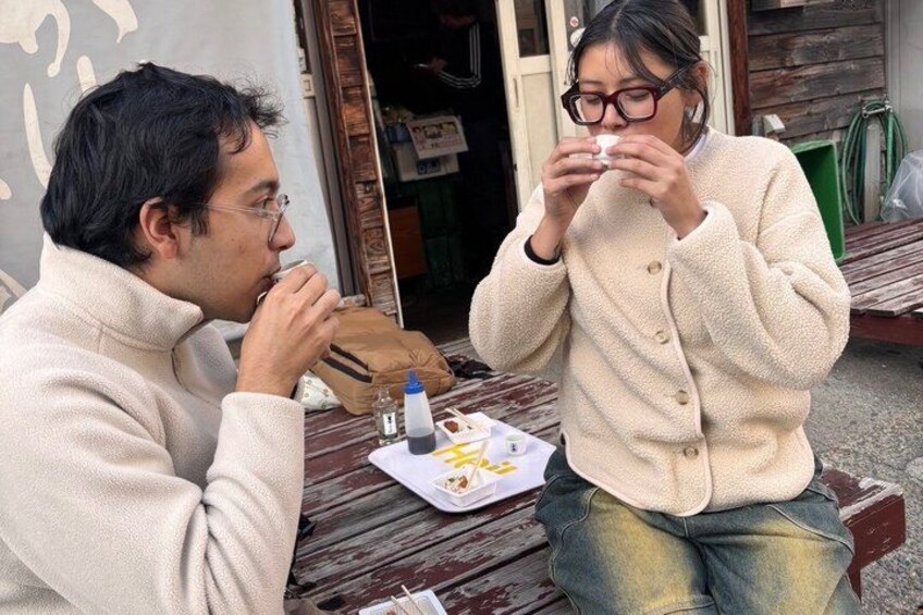 Two people sitting at a wooden table outdoors, eating food. 5