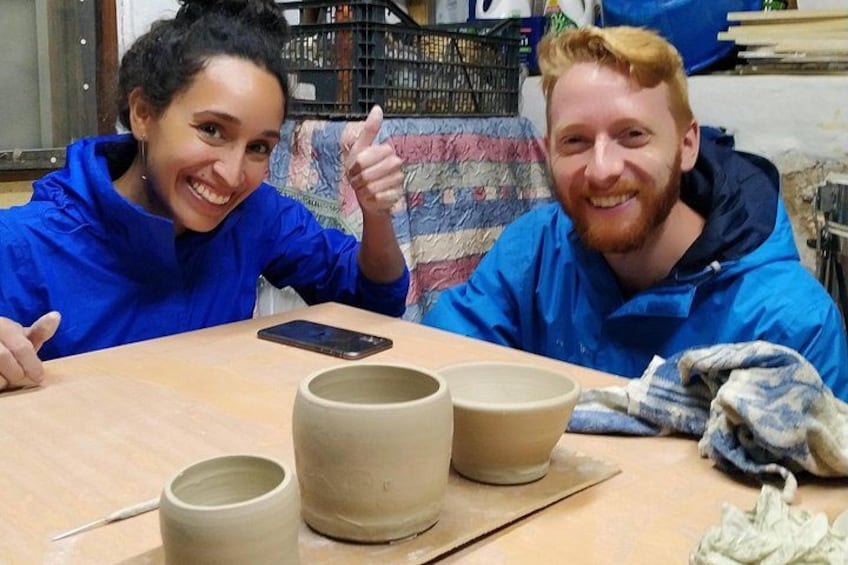 Two people sitting at a table with pottery items and a smartphone. 5