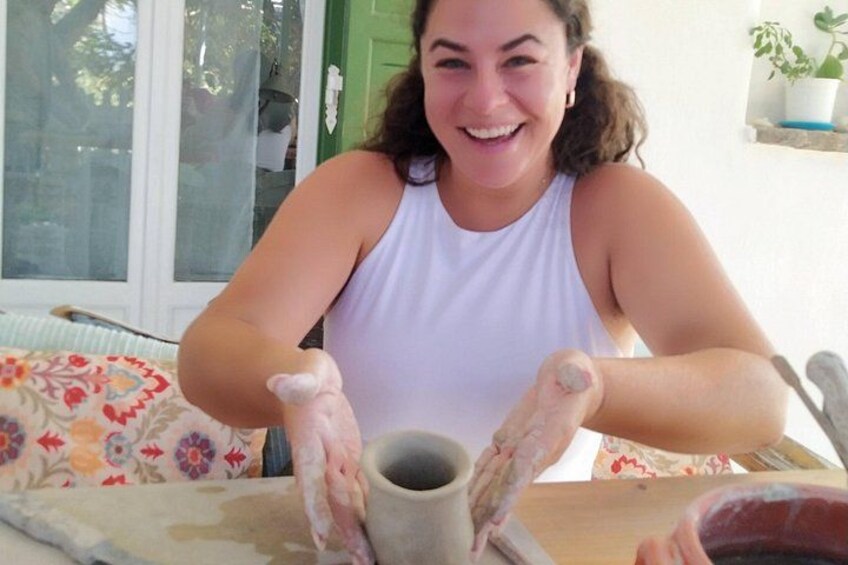 A person engaged in pottery making, with a clay pot in progress and a table covered with a floral tablecloth. 2