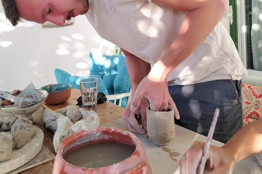 A person working with clay on a table, surrounded by bowls and a glass of water. 3