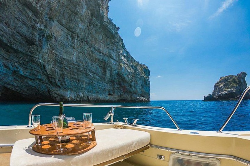 A boat with a table set for two, glasses, and a bottle, surrounded by clear blue water and rocky cliffs. 2