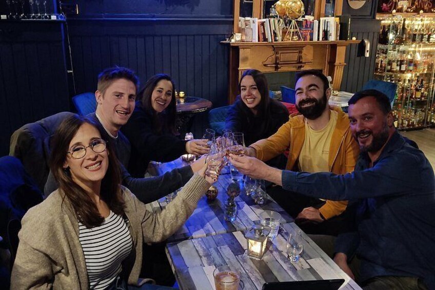 En grupp människor skålar med drinkar vid ett bord på en bar, där det finns hyllor fulla med flaskor. 1