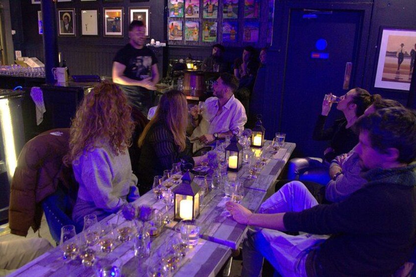 Un bar où des clients sont assis à des tables, avec des verres et des bouteilles devant eux. 2