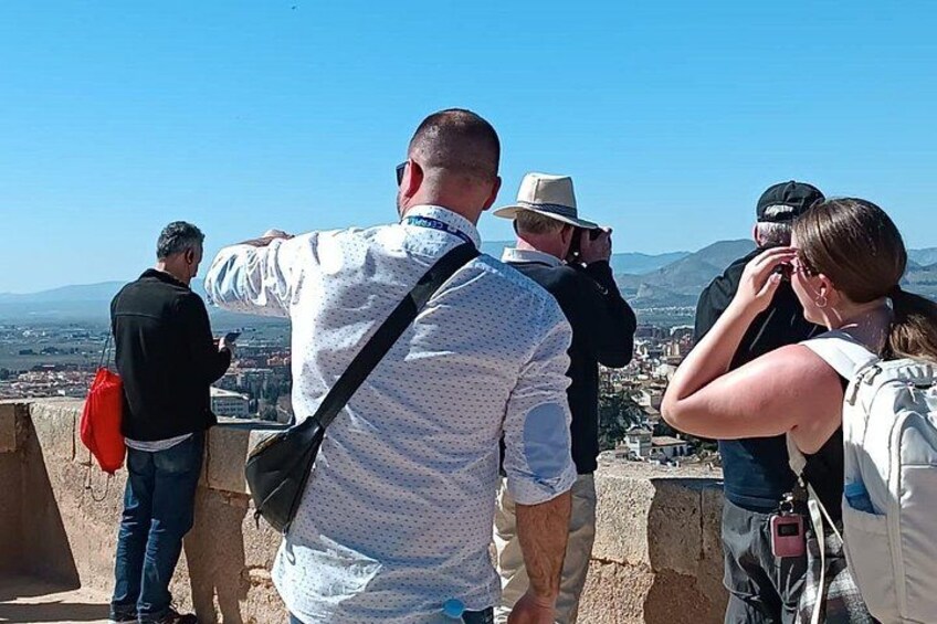 A group of people standing on a viewing platform, overlooking a cityscape with mountains in the distance. 1