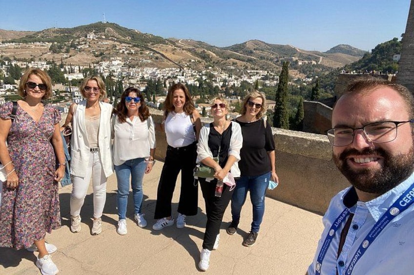 A group of people standing on a terrace with a view of a hilly landscape and a town in the background. 4