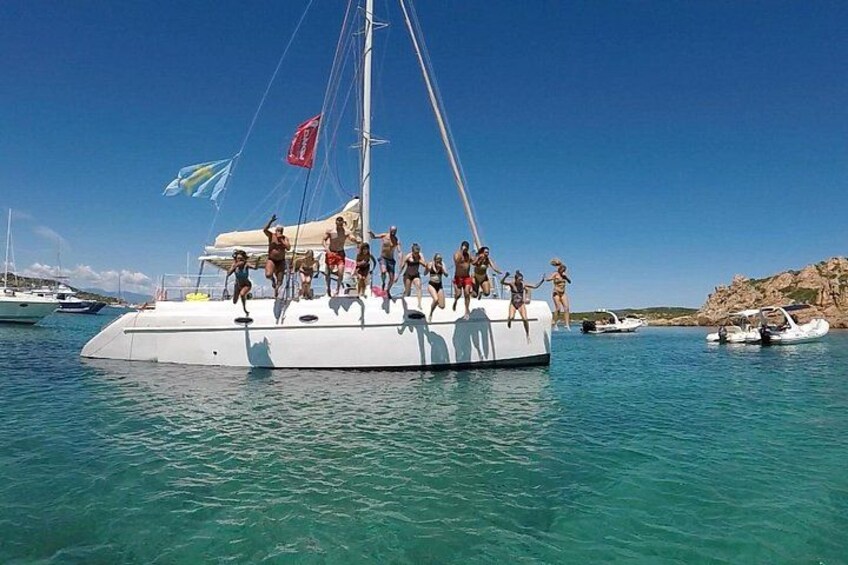 Een zeilboot met mensen aan dek, omringd door kalm blauw water en andere boten. 3