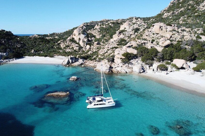 Helder turquoise water, een wit zandstrand, rotsachtige kliffen en een zeilboot voor anker dichtbij de kust. 2