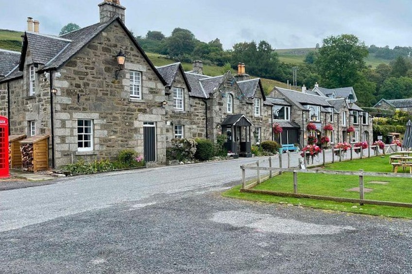 A stone building with a red telephone booth, a grassy area, and a paved road. 2