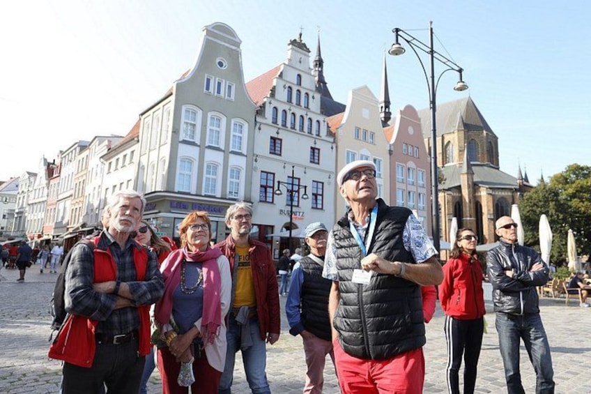 En grupp människor som står på ett torg med kullerstenar, och i bakgrunden syns historiska byggnader. 1
