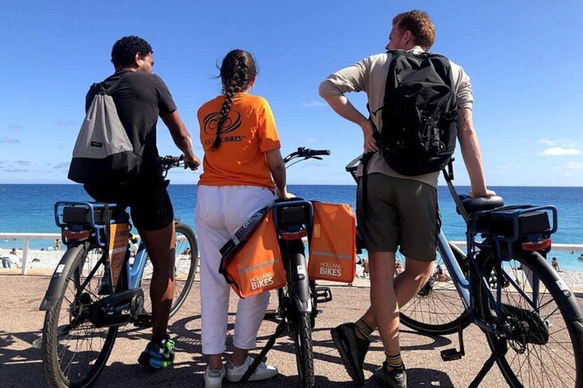 Drei Personen fahren mit Fahrrädern am Strand, im Hintergrund ein klarer Himmel und das Meer. 4