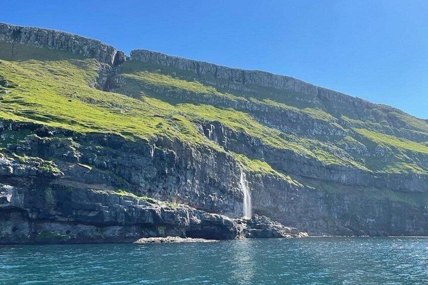 A coastal landscape with a waterfall, green cliffs, and clear blue water. 3