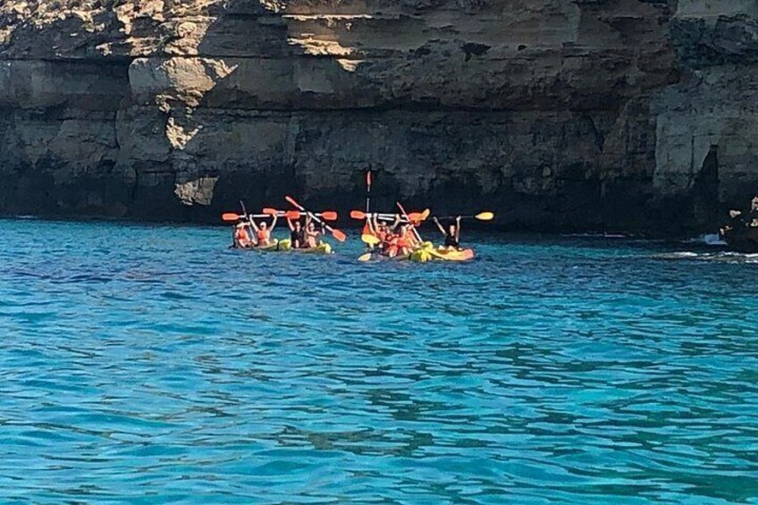 A group of people kayaking on a calm sea with rocky cliffs in the background. 2