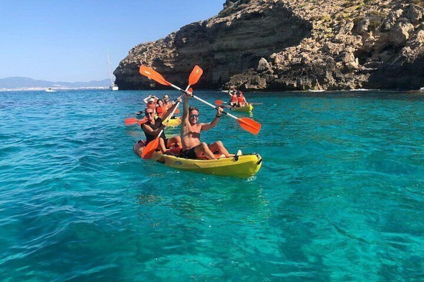 People kayaking on clear turquoise water with rocky cliffs in the background. 3