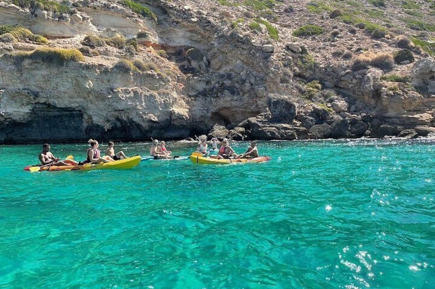 People kayaking on turquoise water with rocky cliffs in the background. 4