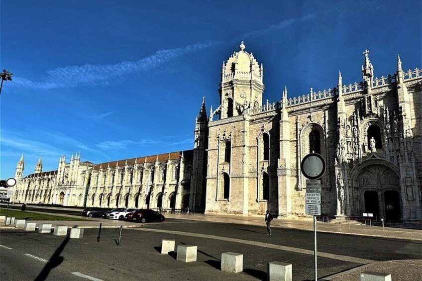 En historisk bygning med detaljeret arkitektur, en klar blå himmel og en vej med autoværn. 3