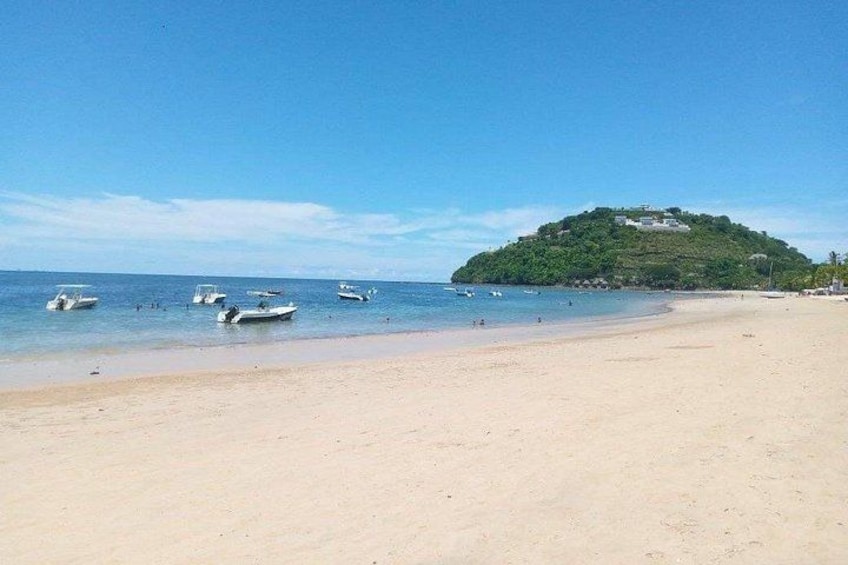 A beach with boats, a sandy shore, and a hill with buildings. 1