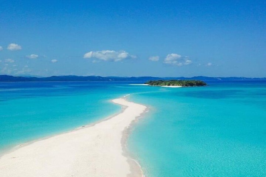 Una playa con aguas turquesas cristalinas, una orilla arenosa y una pequeña isla a lo lejos. 1