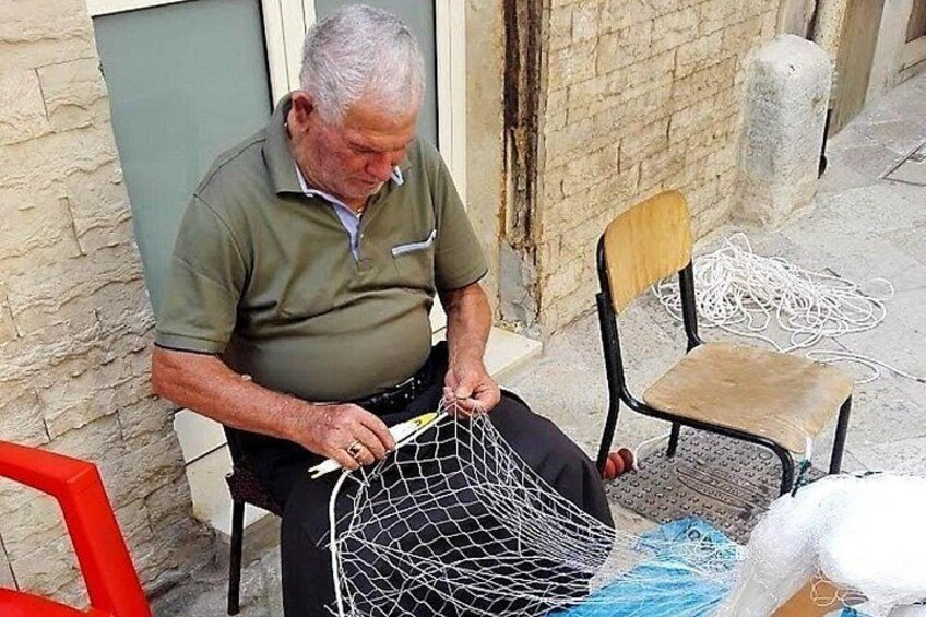 Un uomo anziano seduto su una sedia, intento a lavorare su una struttura in rete metallica. 2