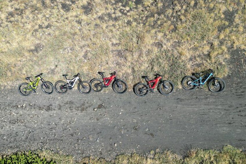 Cinco bicicletas alineadas en un sendero de tierra con una ladera seca y cubierta de hierba al fondo. 3