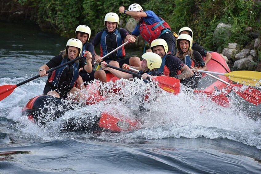 A group of people in a red raft navigating through a river, wearing helmets and life jackets. 2