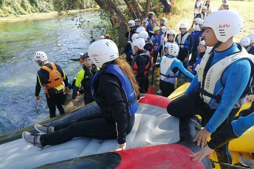 Personen mit Helmen und Schwimmwesten bereiten sich auf eine Rafting-Tour auf einem Fluss vor. 3
