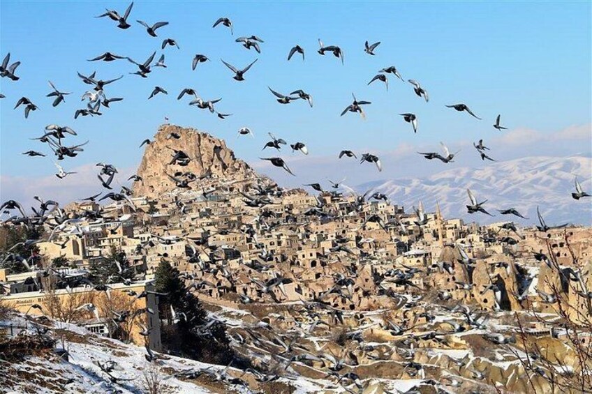 Un pueblo montañoso con un pico rocoso destacado y una bandada de pájaros volando sobre él. 5