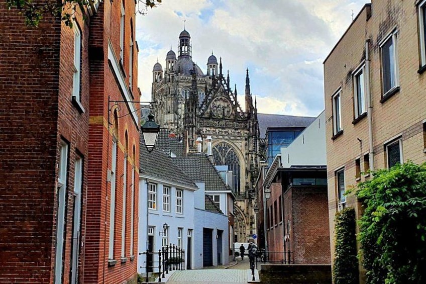 Une rue étroite bordée de bâtiments historiques, une église dont le clocher est particulièrement imposant, et un cycliste au premier plan. 4